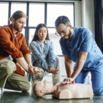 professional paramedic in eyeglasses and uniform showing chest compressions on CPR manikin near