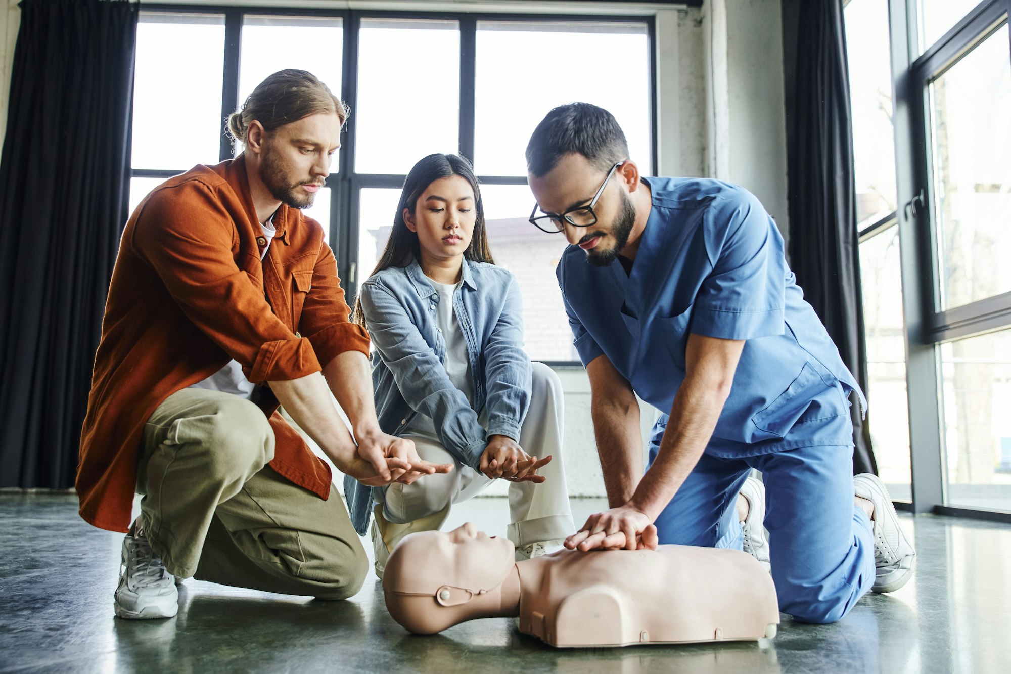 professional paramedic in eyeglasses and uniform showing chest compressions on CPR manikin near
