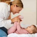 Child care. Happy woman making gymnastics to her baby girl, playing and bonding with infant